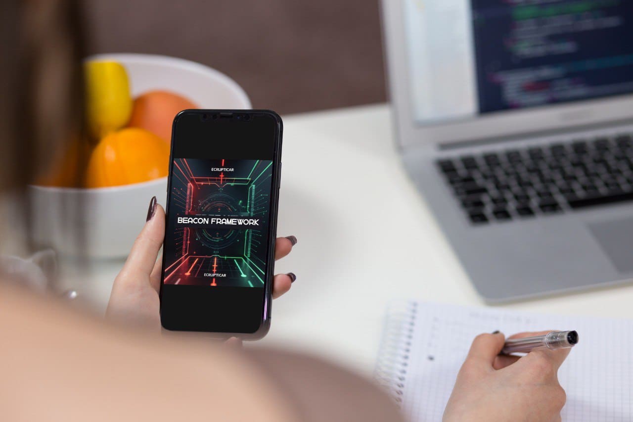 Person holding a smartphone with a screen displaying 'Beacon Framework' in an office setting.