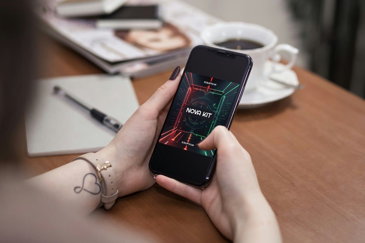Person holding a smartphone with a 'NOVA KIT' course on a table with a coffee cup and notebook.
